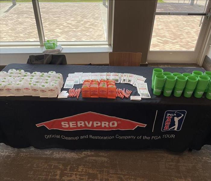 a picture of a table set up with a SERVPRO table cloth, green cups, personal restoration kits, and our orange pens. 